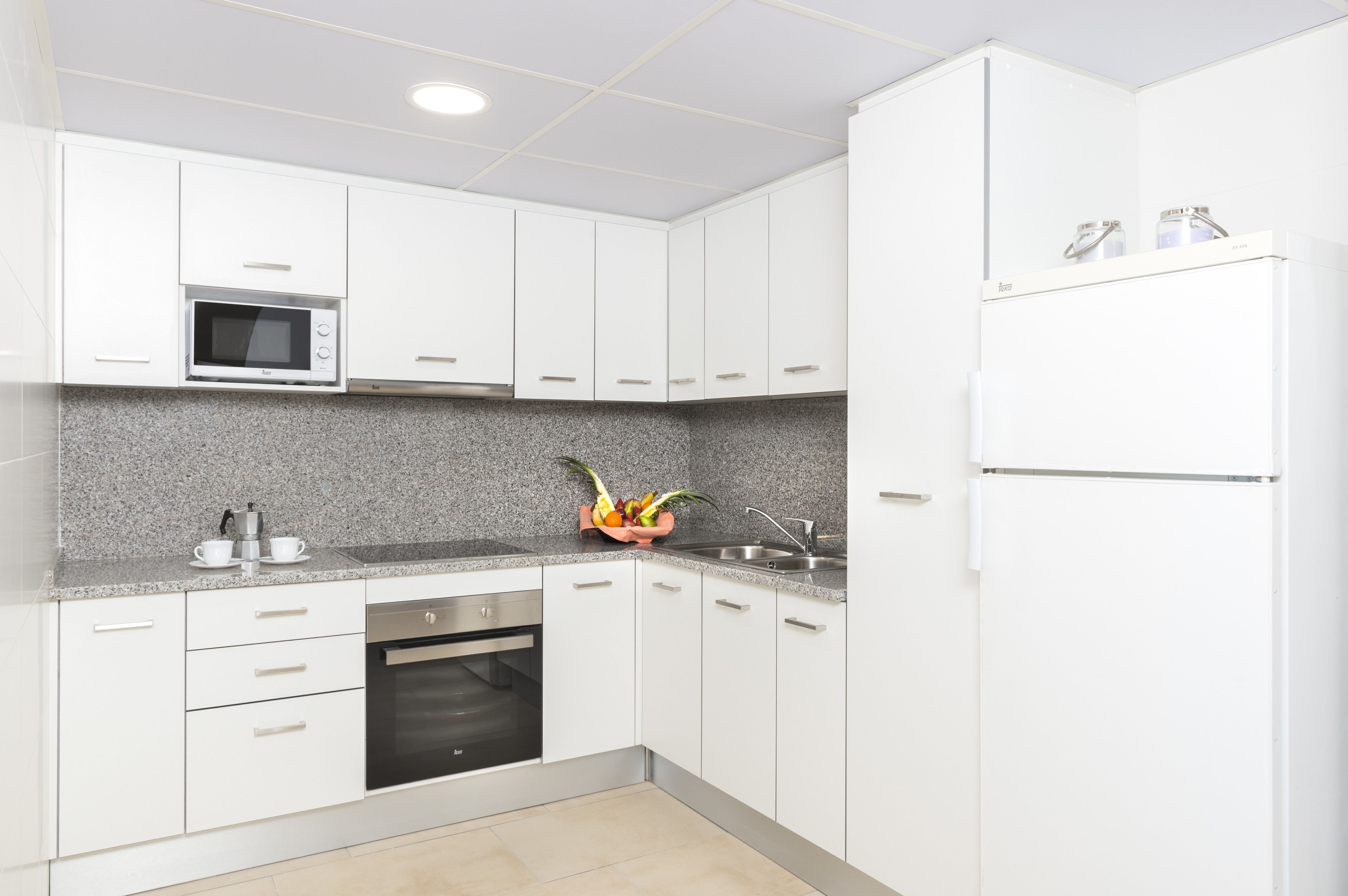 Una cocina moderna con armarios blancos, microondas, horno empotrado y refrigerador.