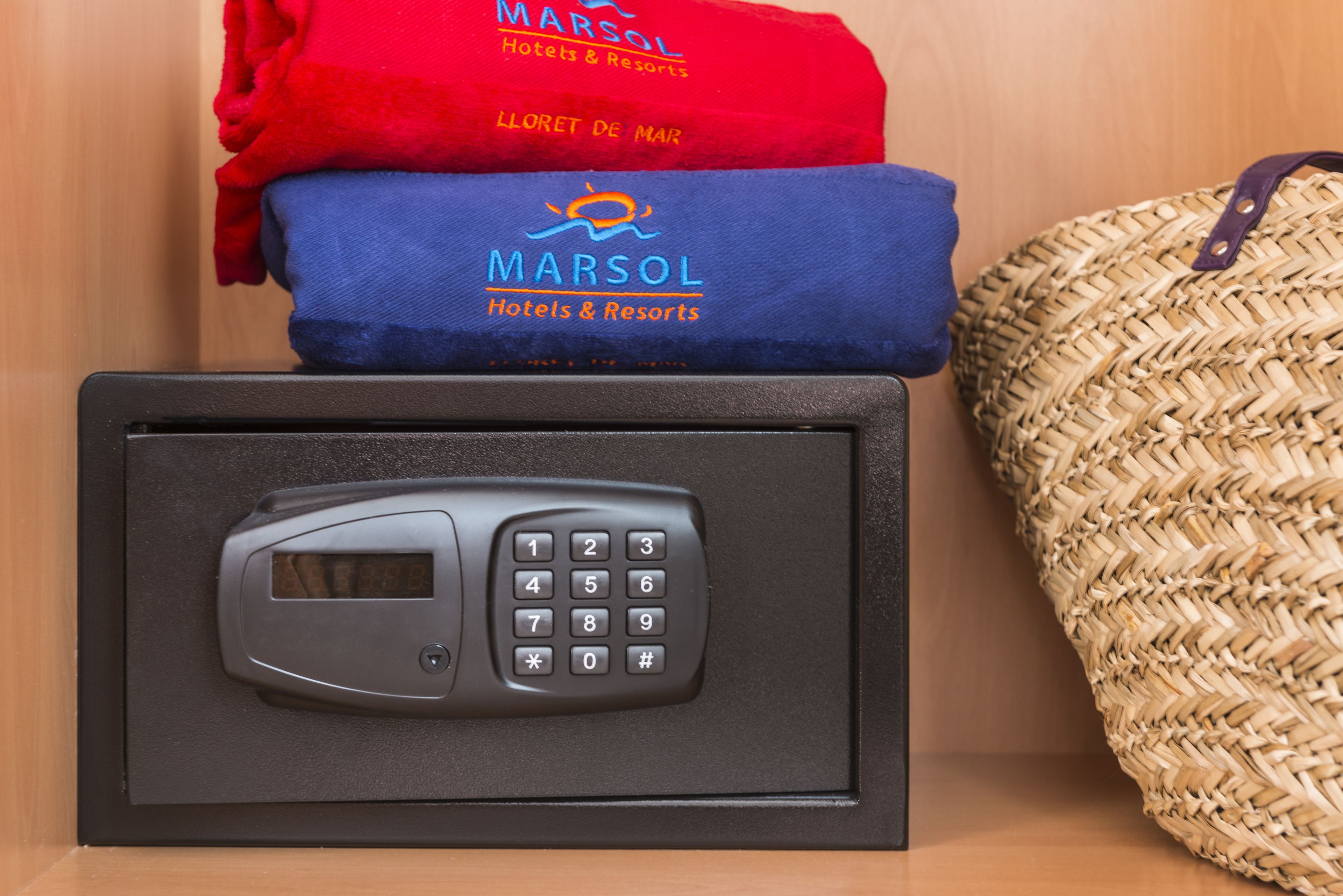 Un panel de teclado de seguridad, una toalla roja y azul con el logotipo de 'Marsol Hotels & Resorts', y un bolso tejido.