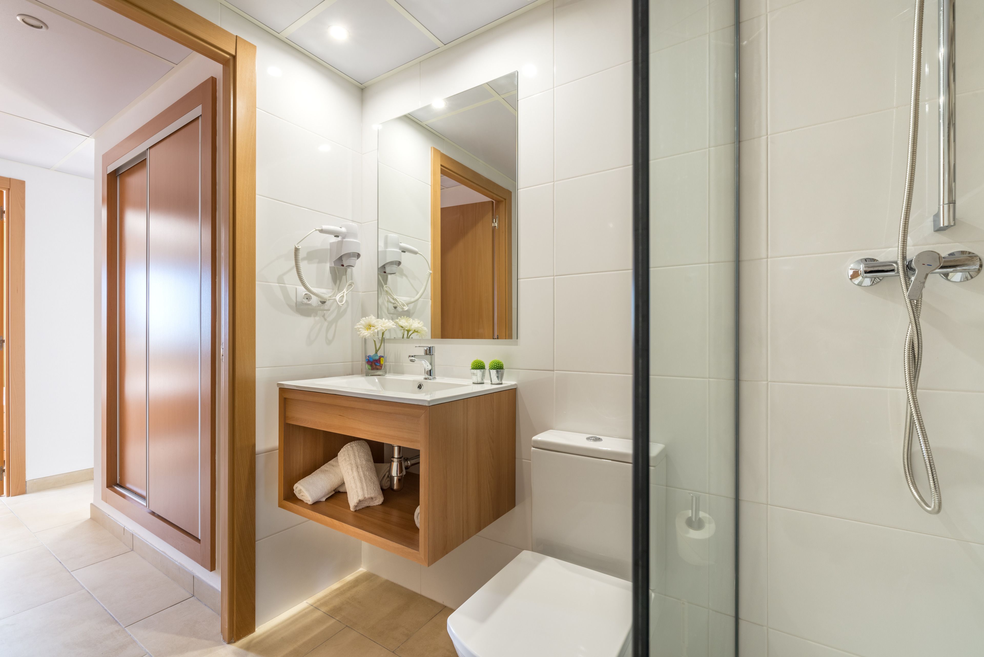 A modern bathroom with a wooden vanity, a large mirror, a toilet, and a shower area.