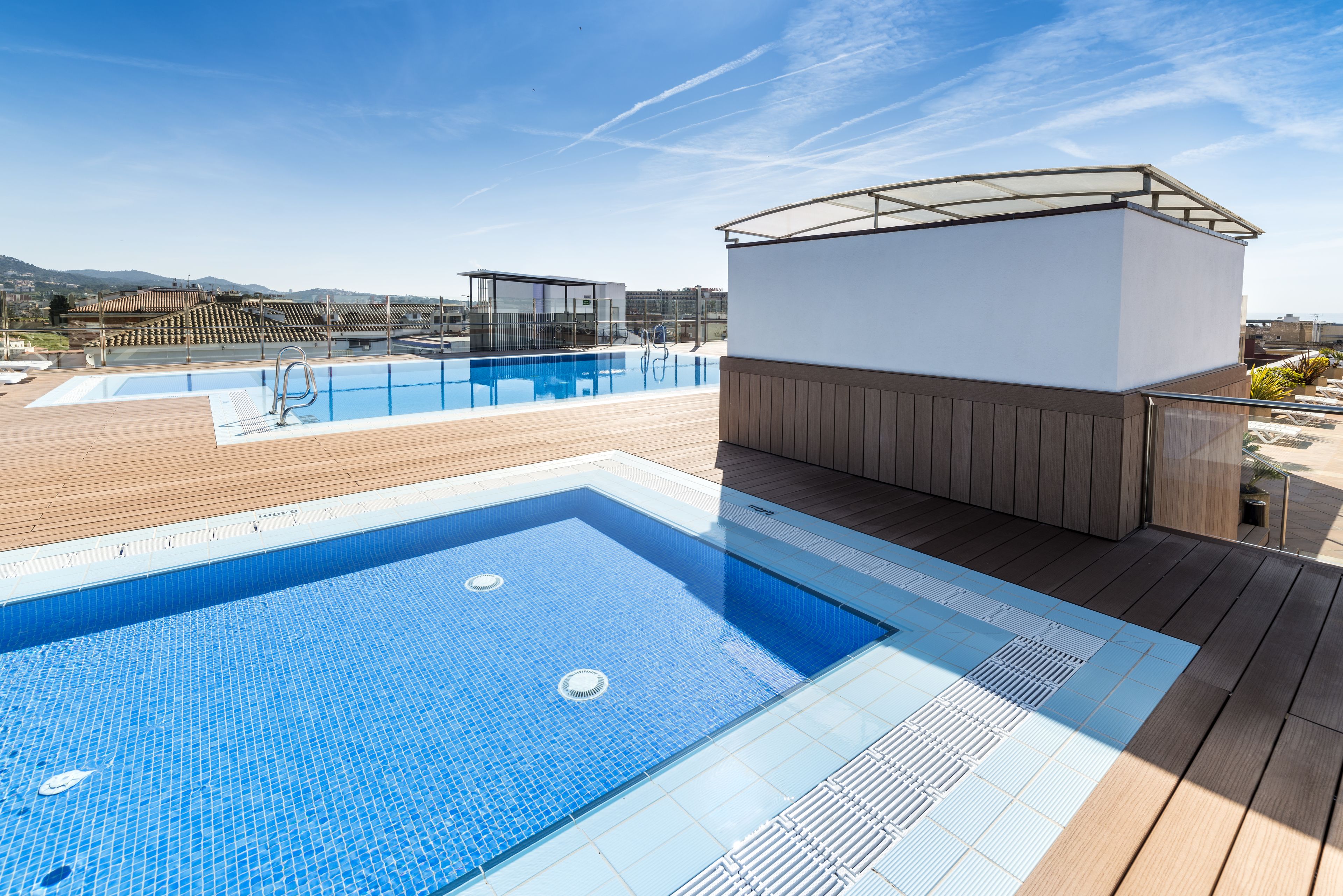 A rooftop swimming pool with a wooden deck and a glass-enclosed hot tub.