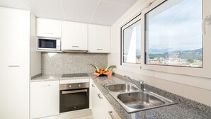 A modern kitchen with white cabinets, a granite countertop, stainless steel sink, and a microwave. - Apartaments Condado (Lloret de Mar)