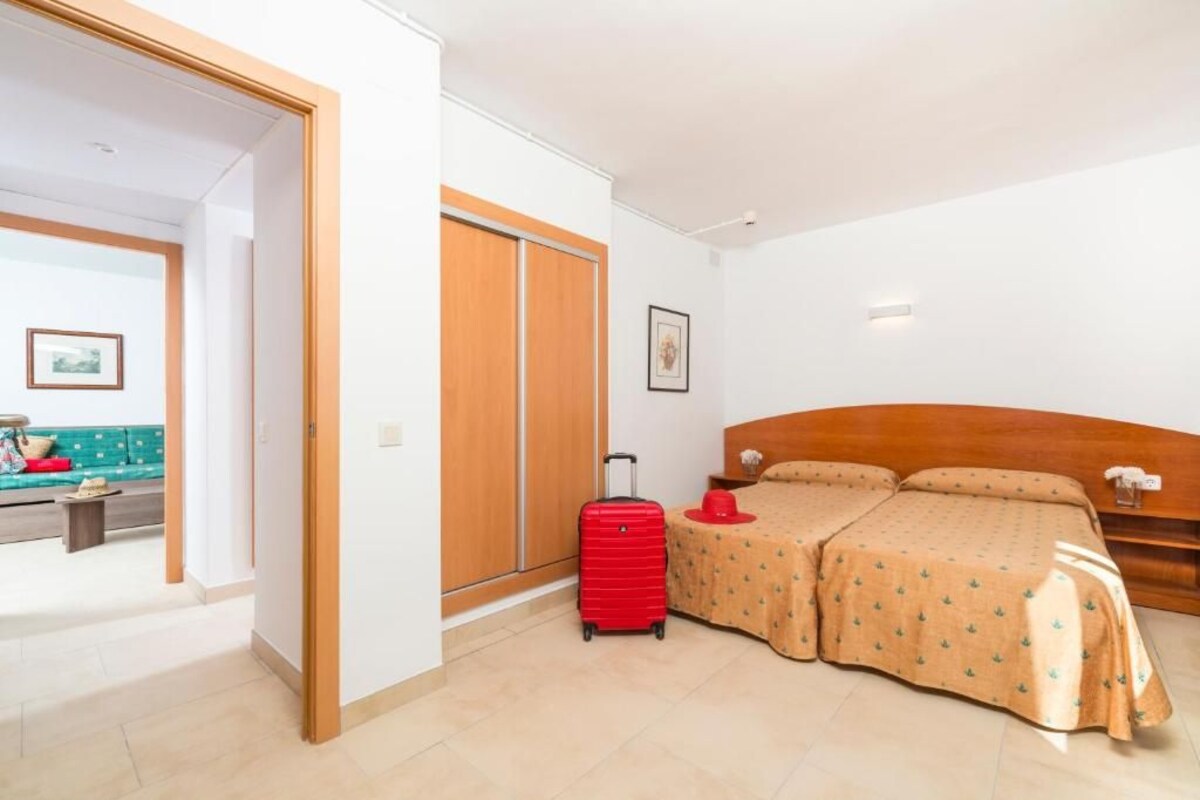Une chambre d’hôtel avec un lit, une valise, une petite table avec une lampe et une armoire.