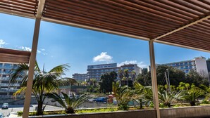 A covered outdoor area with a view of a multi-story building labeled "COSTA ENCANTADA" in the background. - Apartaments Condado (Lloret de Mar)