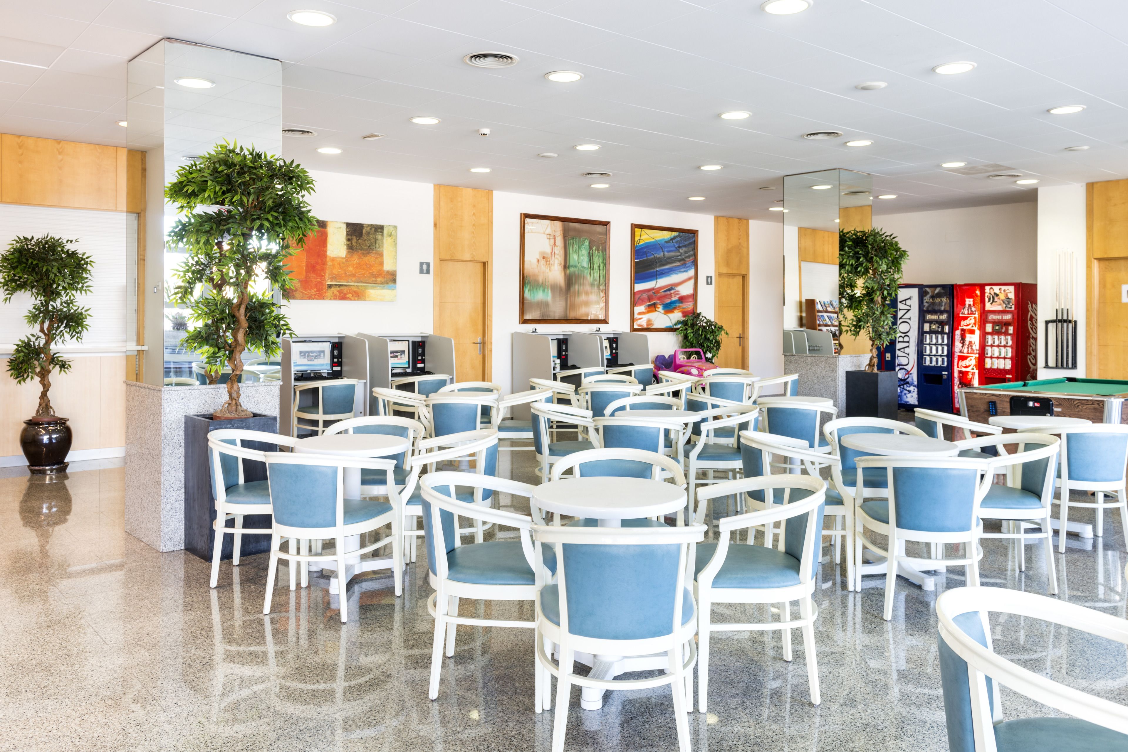 A spacious indoor area with multiple seating arrangements, including tables and chairs, and several potted plants.
