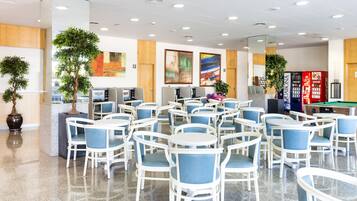A spacious indoor area with multiple seating arrangements, including tables and chairs, and several potted plants.