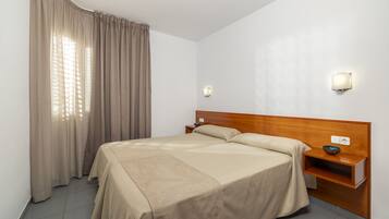 A neatly made bed with a wooden headboard, a bedside table with a bowl, and a wall-mounted light fixture.