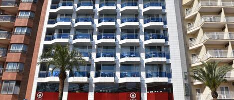 Un hotel de varios pisos con balcones, un toldo rojo y un letrero visible de 'SPAR'.