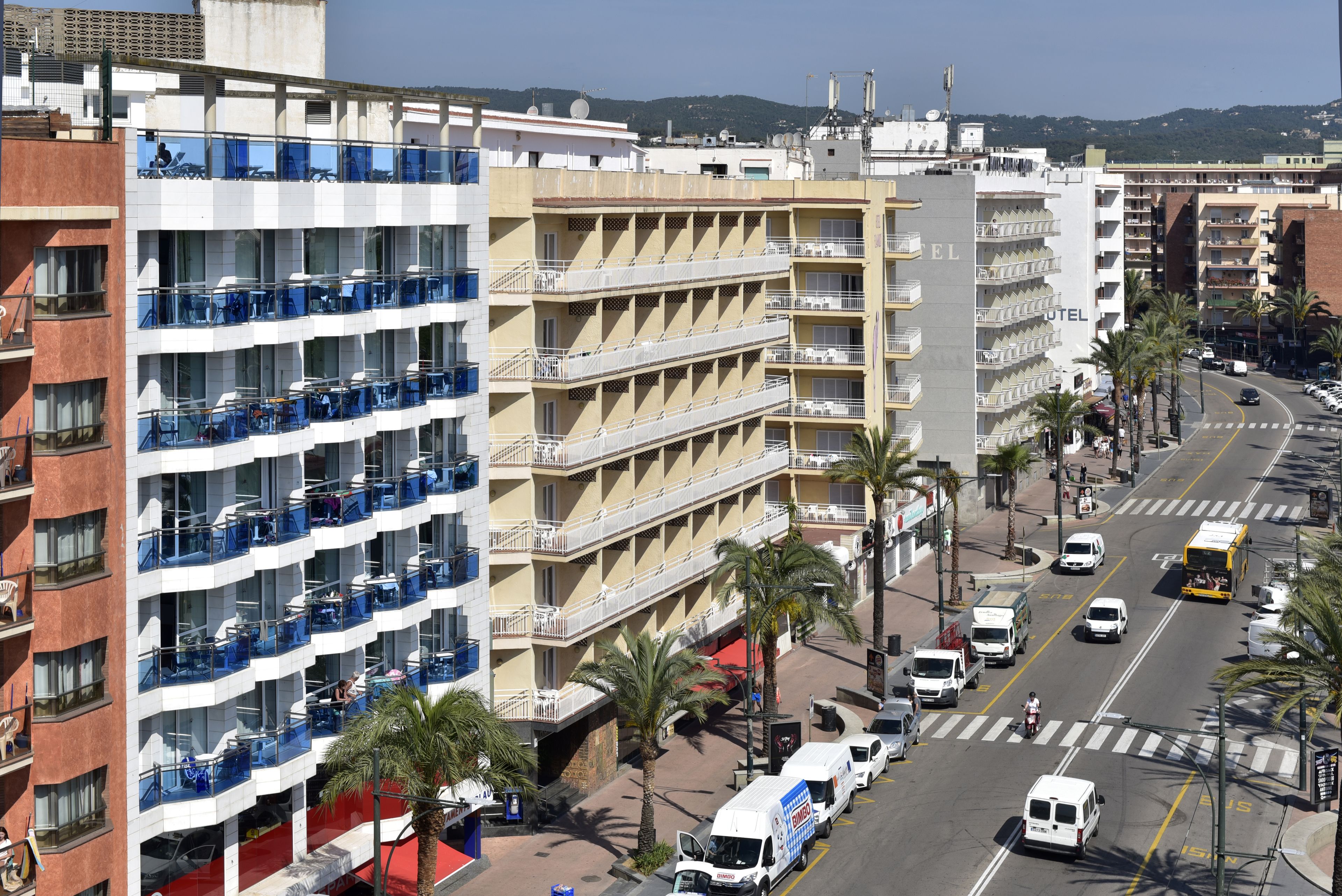A multi-story hotel with balconies, a red carpet entrance, and a street view with vehicles and palm trees.
