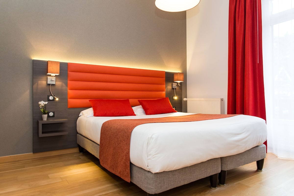 Ein modernes Hotelzimmer mit einem großen Bett, einem Nachttisch mit Lampe und einem roten Vorhang.