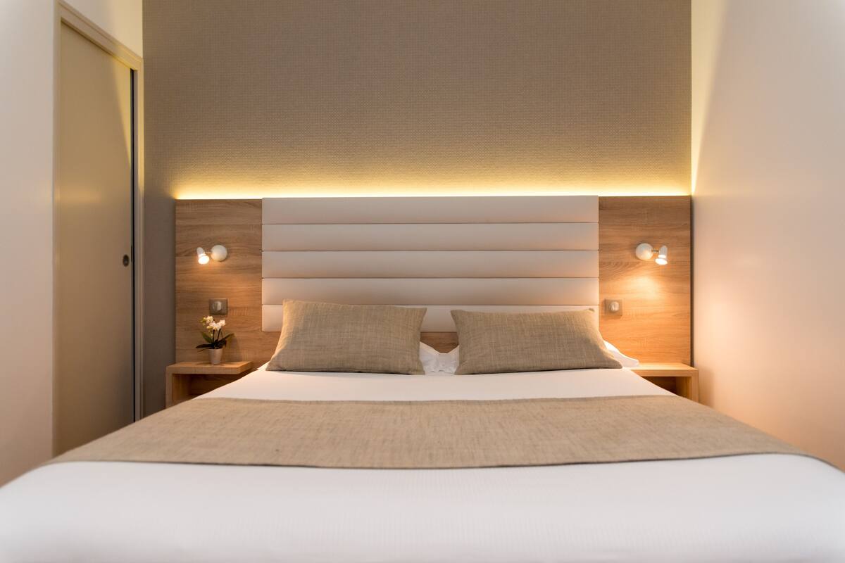 Ein modernes Hotelzimmer mit einem großen Bett, zwei Nachttischen und einem Kopfteil mit integrierter Beleuchtung.