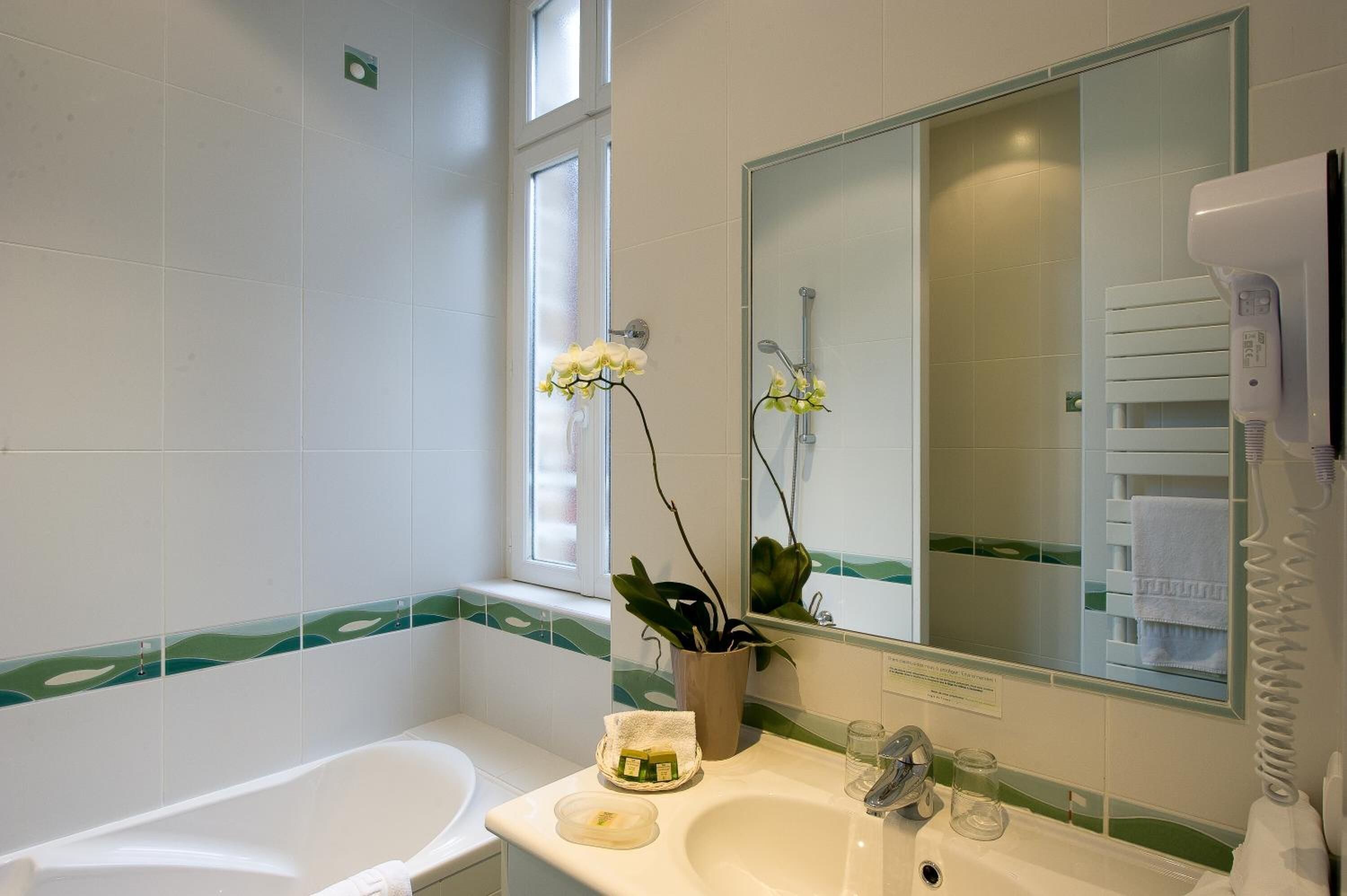 Une salle de bain équipée d’une baignoire, d’un lavabo, d’un miroir et d’un sèche-cheveux.