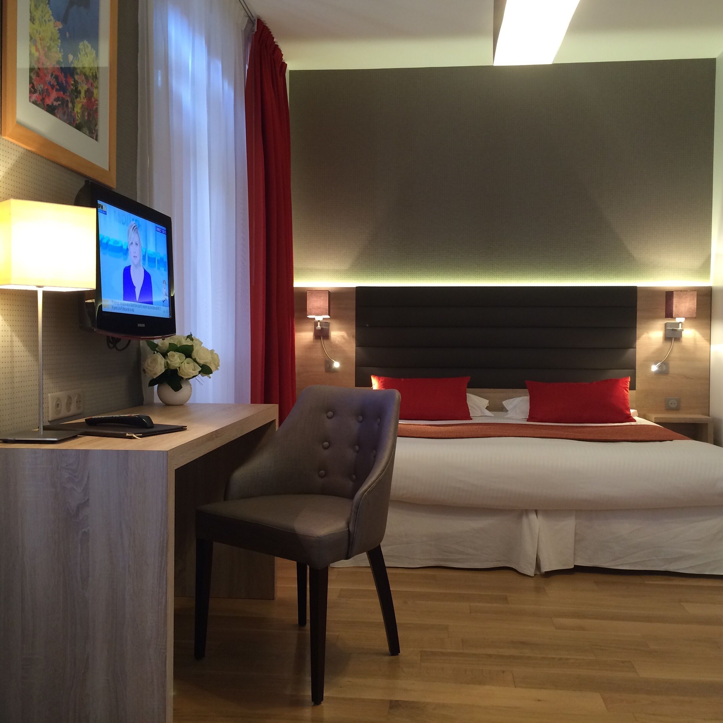 Une chambre d’hôtel équipée d’un lit, d’un bureau avec un ordinateur, d’une chaise et d’un téléviseur diffusant une chaîne d’information.
