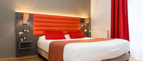 A modern hotel room with a large bed, orange headboard, and red curtains.