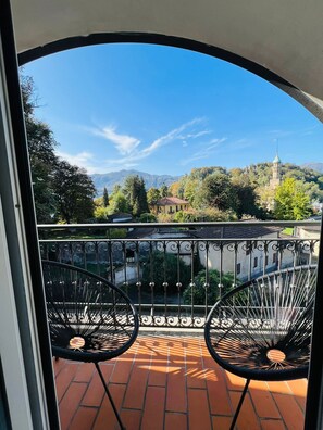 A balcony with wrought iron chairs, a tiled floor, and a view of a mountain and a church. - Hotel Santa Caterina (Orta San Giulio)