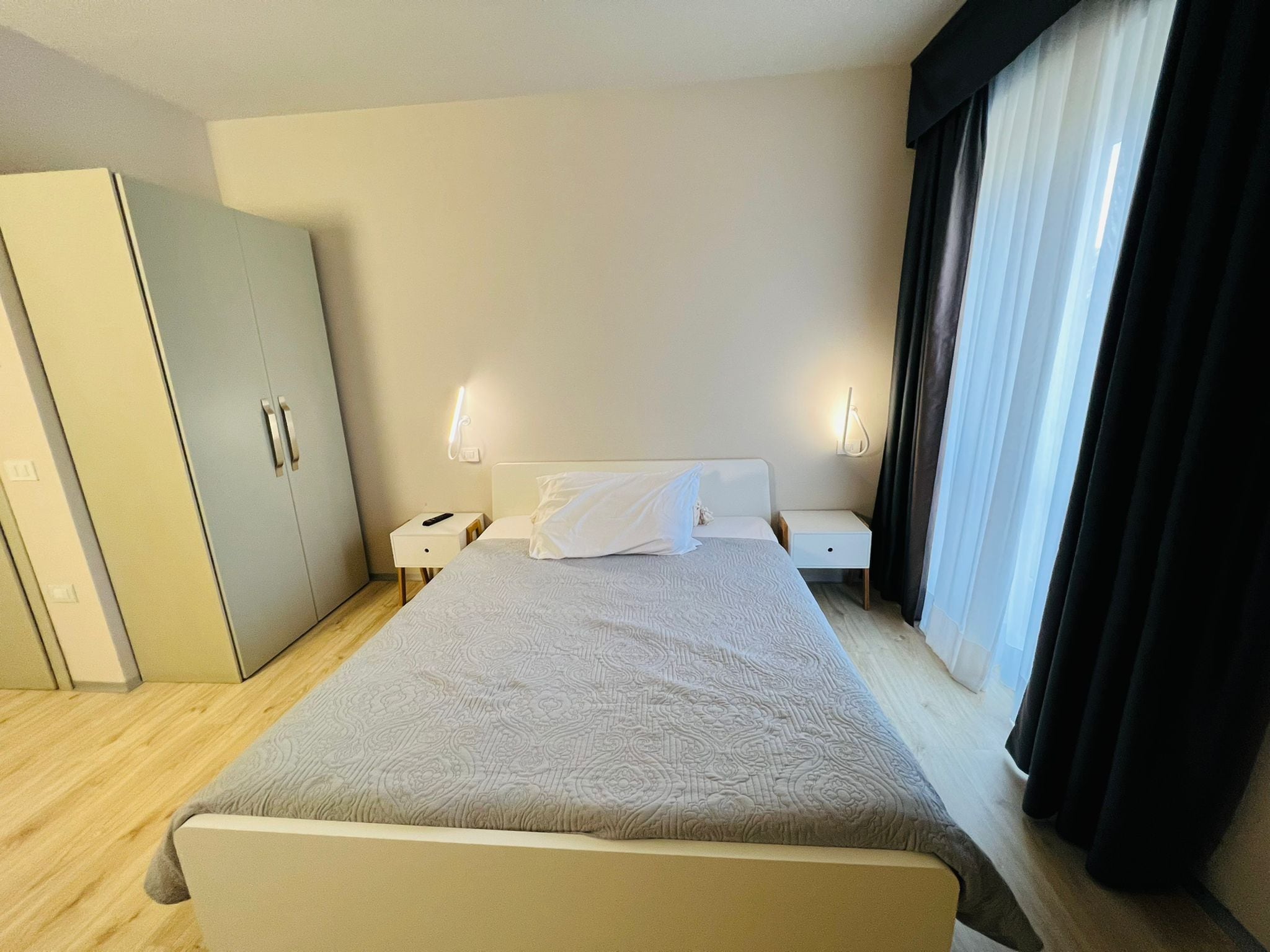 Hotellihuone, jossa on suuri sänky, kaksi yöpöytää, vaatekaappi ja ikkuna, jossa on verhot.