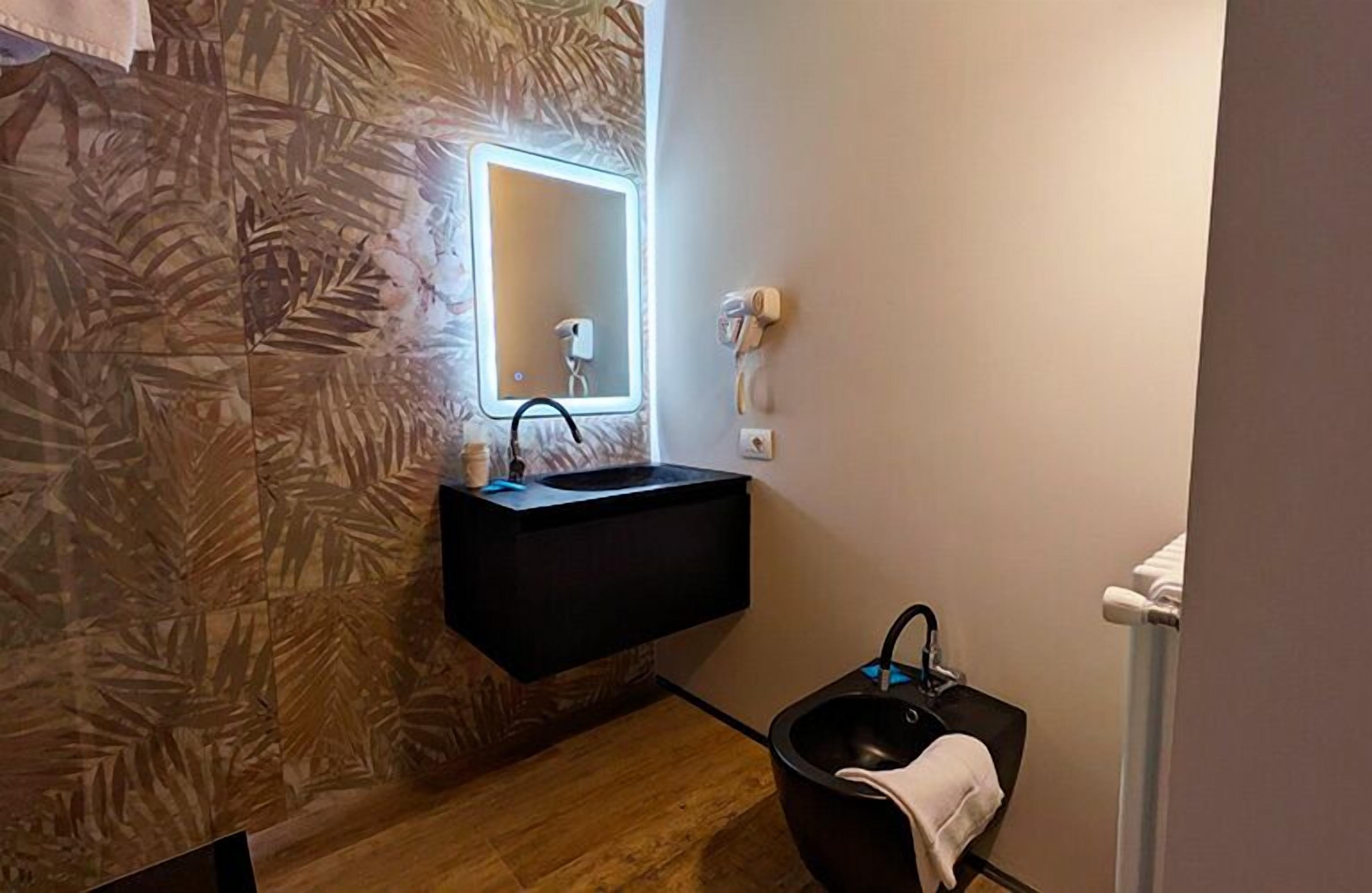 A bathroom with a black sink, a mirror with a light, a towel rack, and a shower area.
