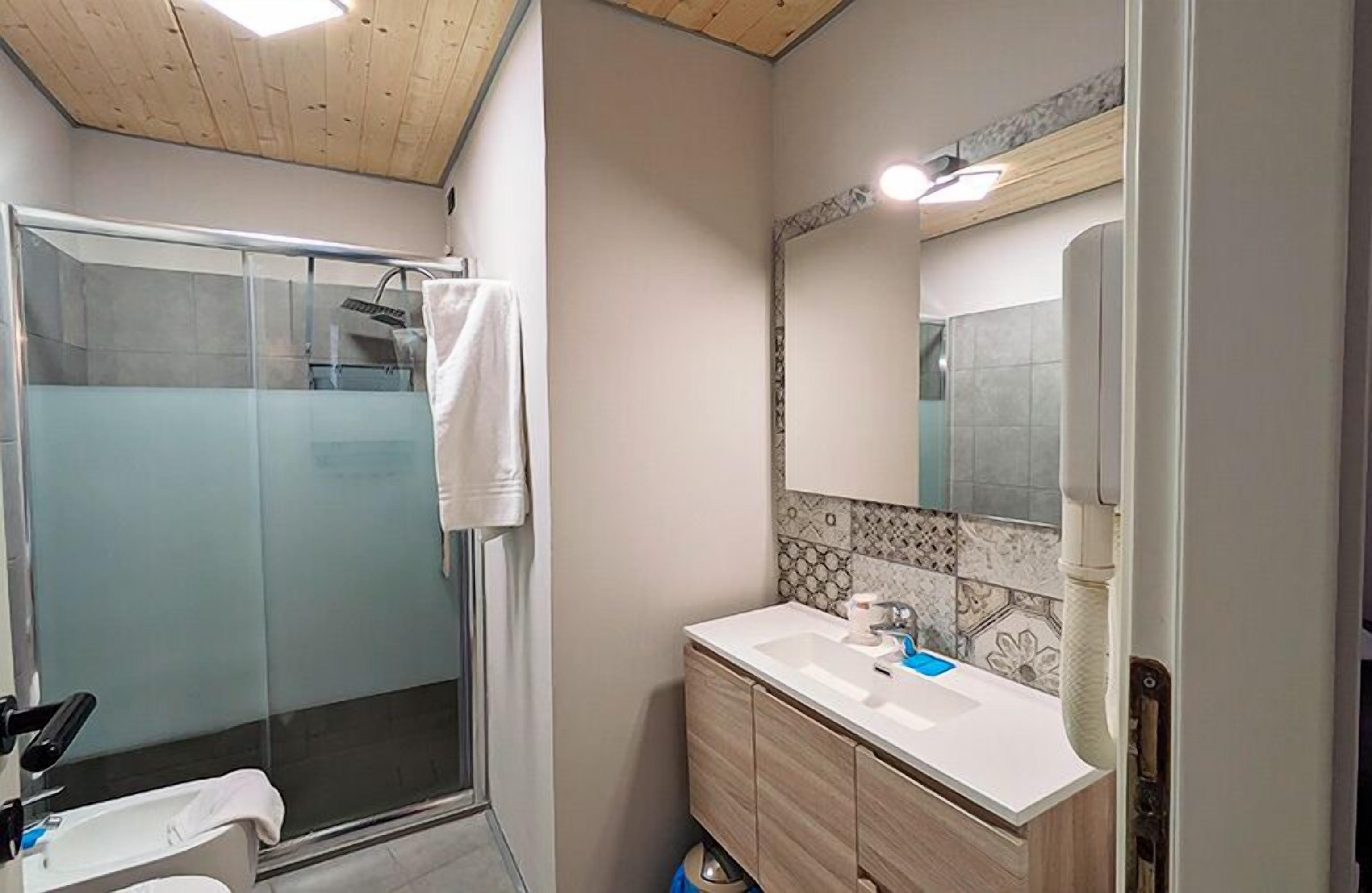 Un baño con cabina de ducha de vidrio, un lavamanos blanco y un espejo con resalte de azulejos decorativos.