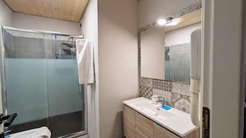 Un baño con cabina de ducha de vidrio, un lavamanos blanco y un espejo con resalte de azulejos decorativos.