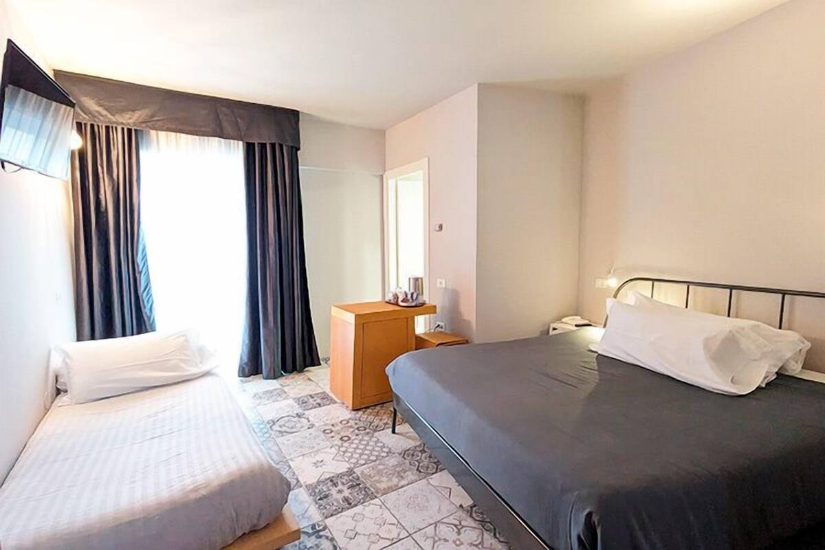 A hotel room with two beds, a nightstand, a dresser, and a mirror.