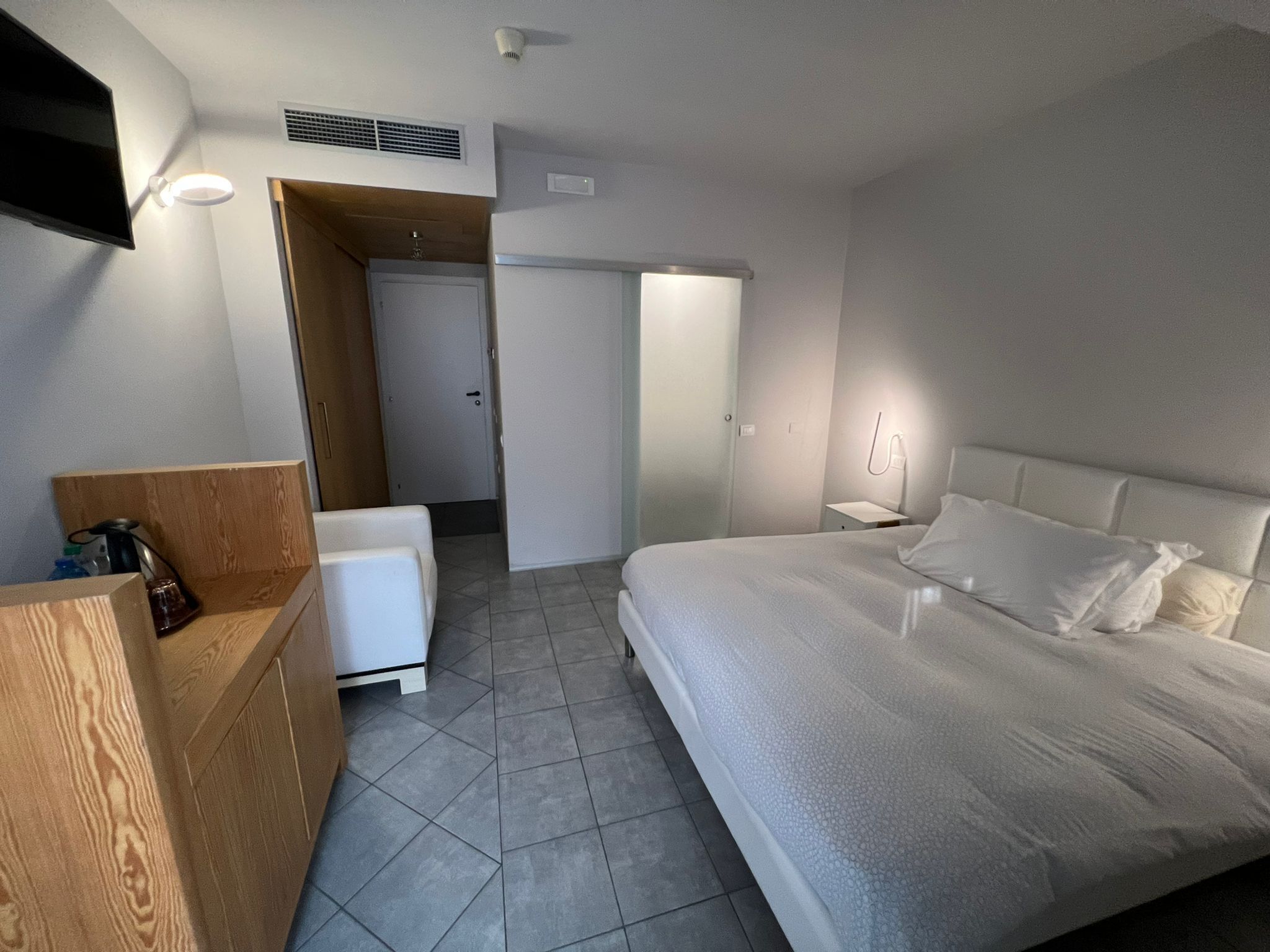 Habitació d'hotel moderna amb un llit gran, una taula de fusta, una televisió i un bany visible a través d'una porta oberta.