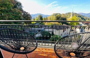 A balcony with two black chairs, a tiled floor, and a view of a mountain and a mosque. - Hotel Santa Caterina (Orta San Giulio)
