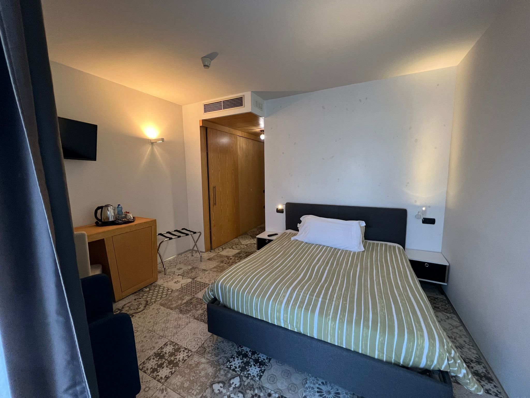 Una camera d'albergo con un letto, una scrivania, una sedia, una televisione e un armadio.