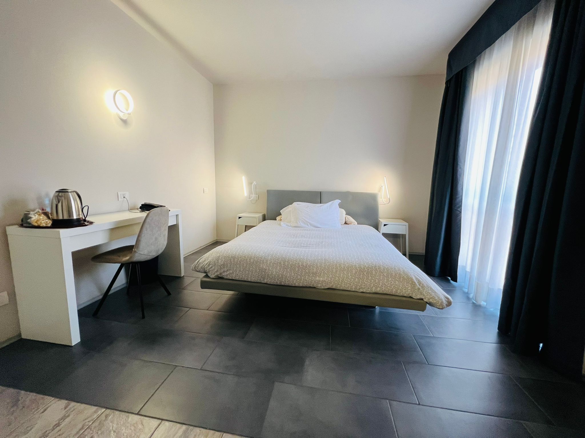 Una habitación de hotel moderna con una cama, un escritorio, una silla y un hervidor.