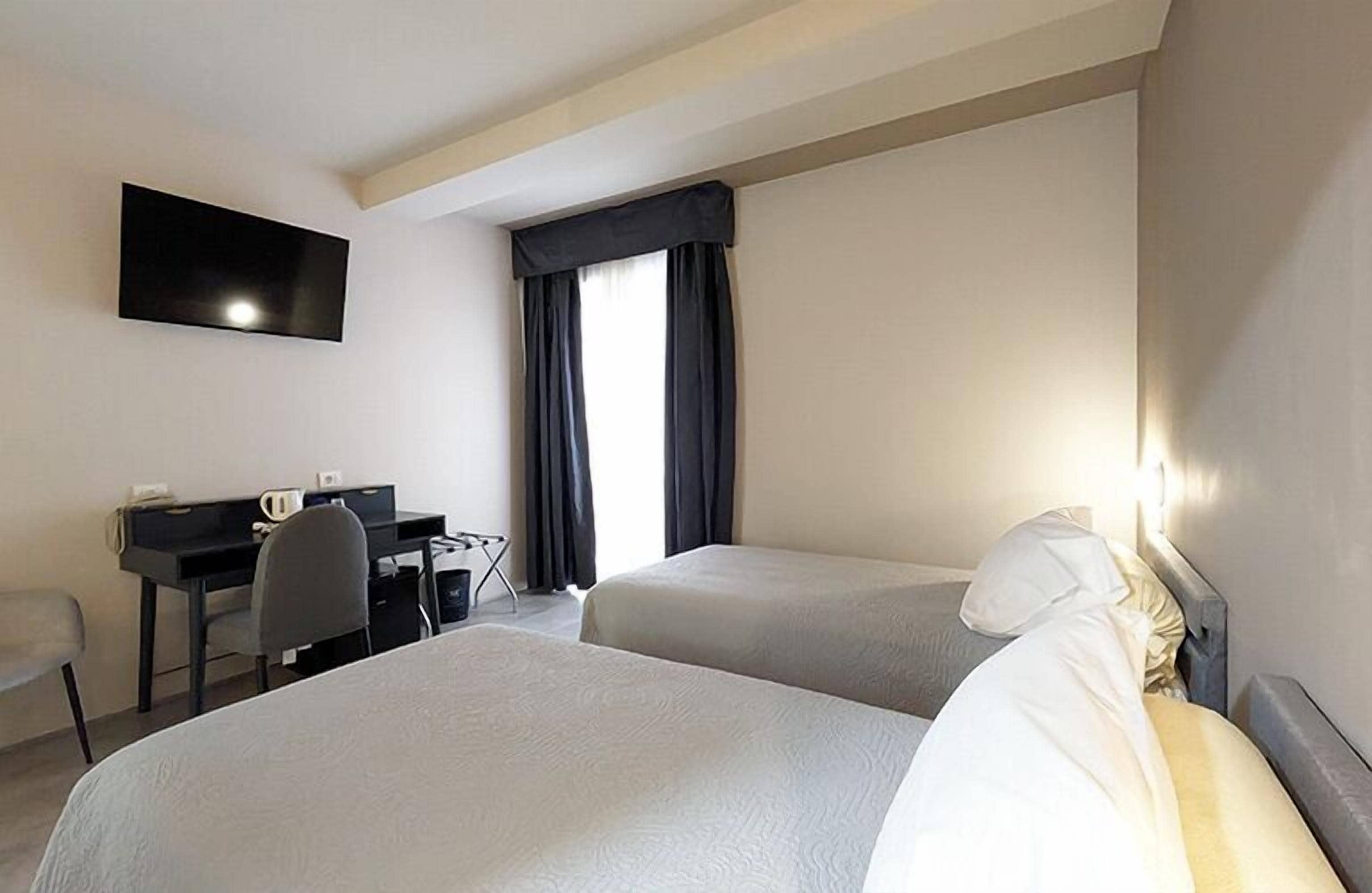 Een hotelkamer met twee eenpersoonsbedden, een bureau met stoel, een wandtelevisie en een raam met donkere gordijnen.