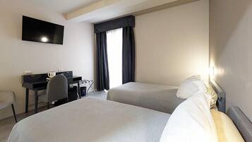 Een hotelkamer met twee eenpersoonsbedden, een bureau met stoel, een wandtelevisie en een raam met donkere gordijnen.