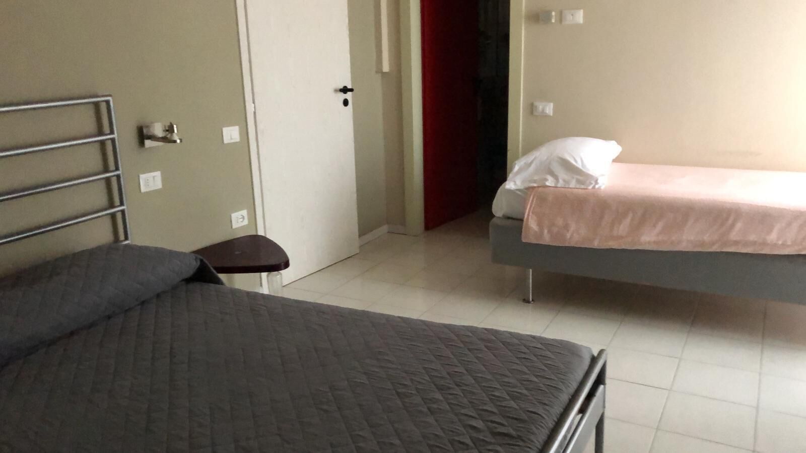 A bedroom with a large bed, a smaller bed, a bedside table, and a door.