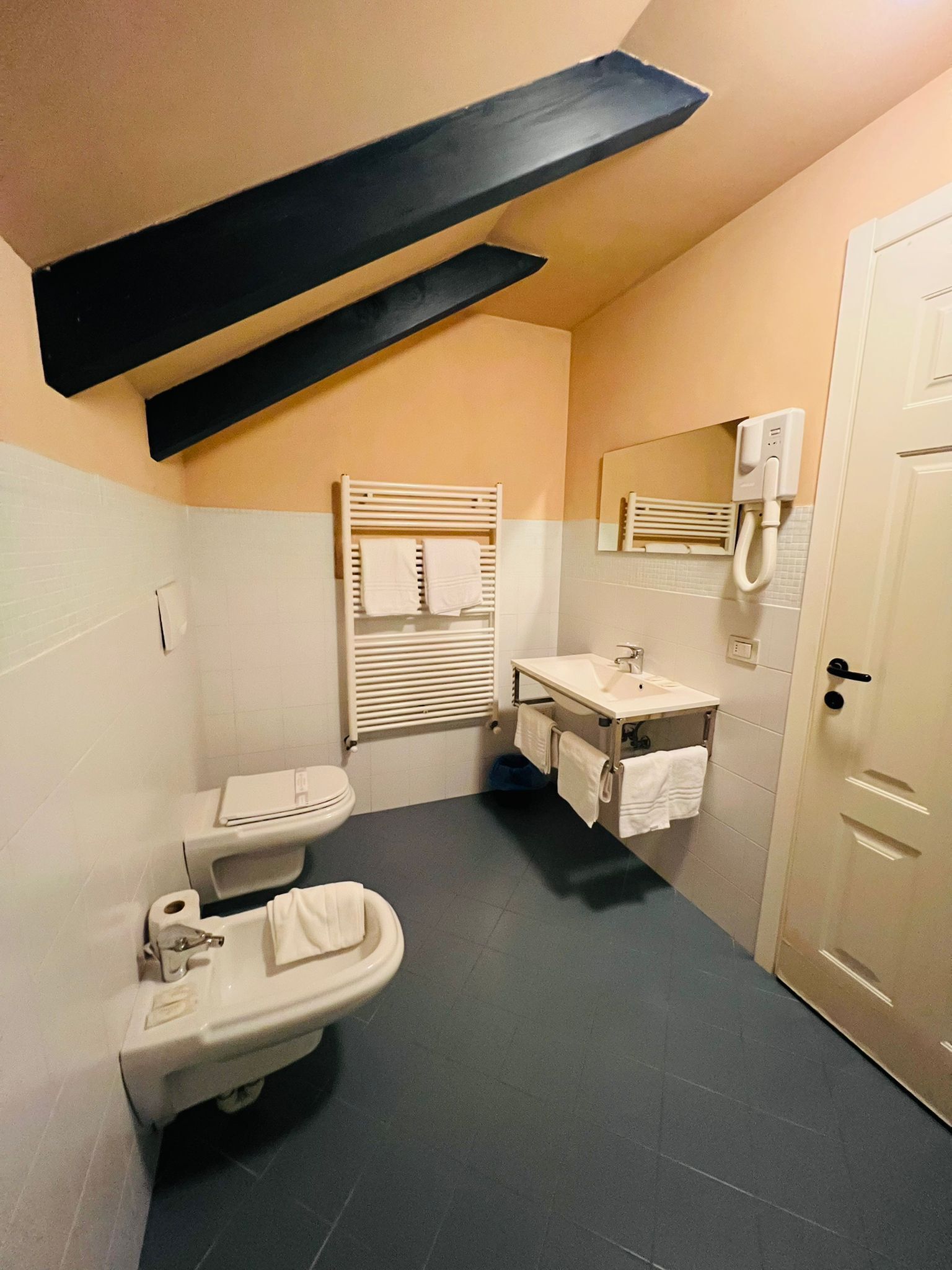 Bany compacte amb vàter, bidet i rentapel, amb sostre de bigues negres i porta blanca.