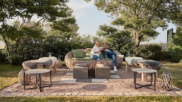 Un área de estar al aire libre acogedora con mobiliario de mimbre y una chimenea central.