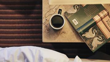 A bed with white bedding, a cup of coffee, and a book on a table.