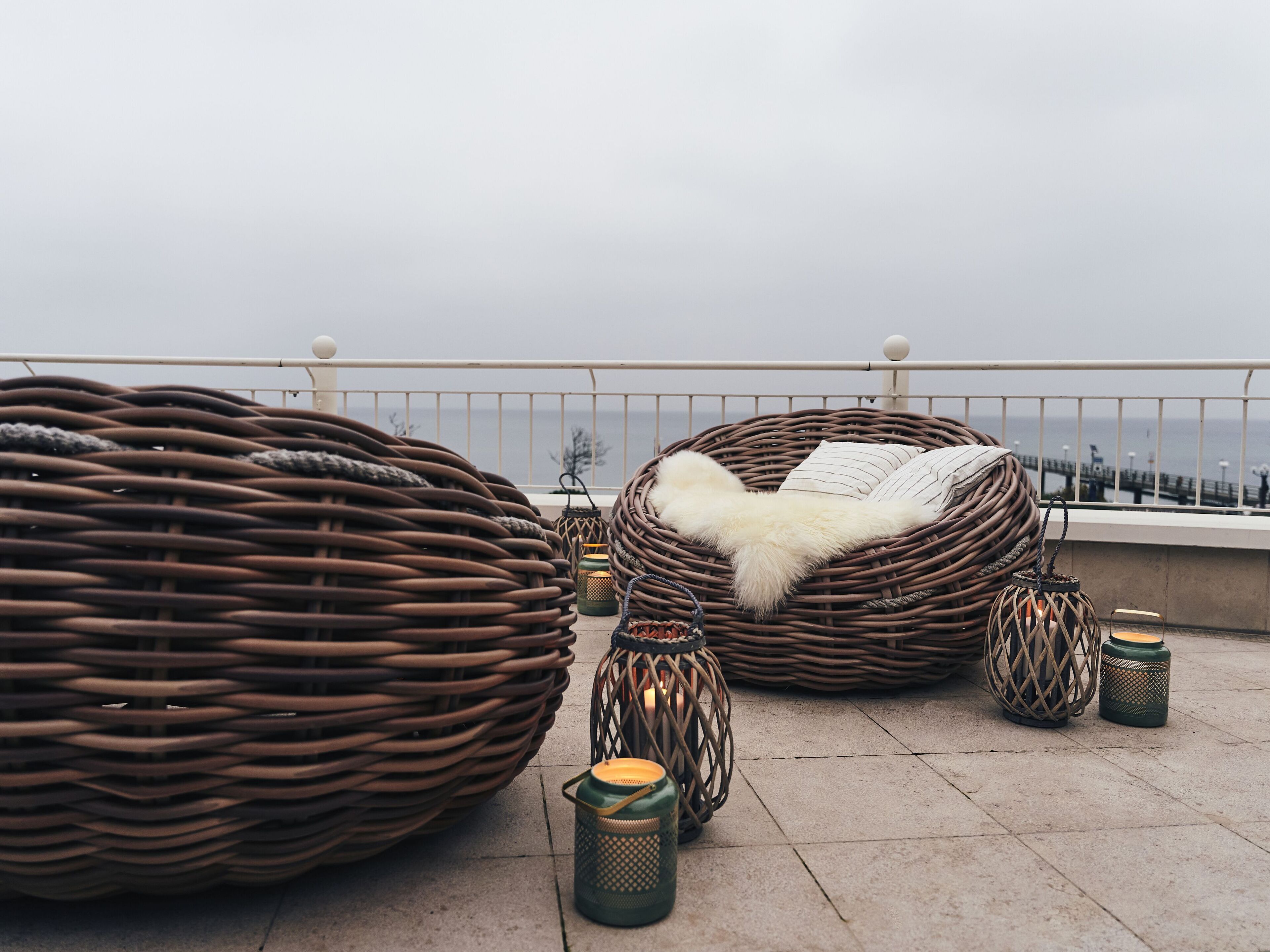 Wicker furniture and lanterns on a balcony with a railing and a view of the sea.