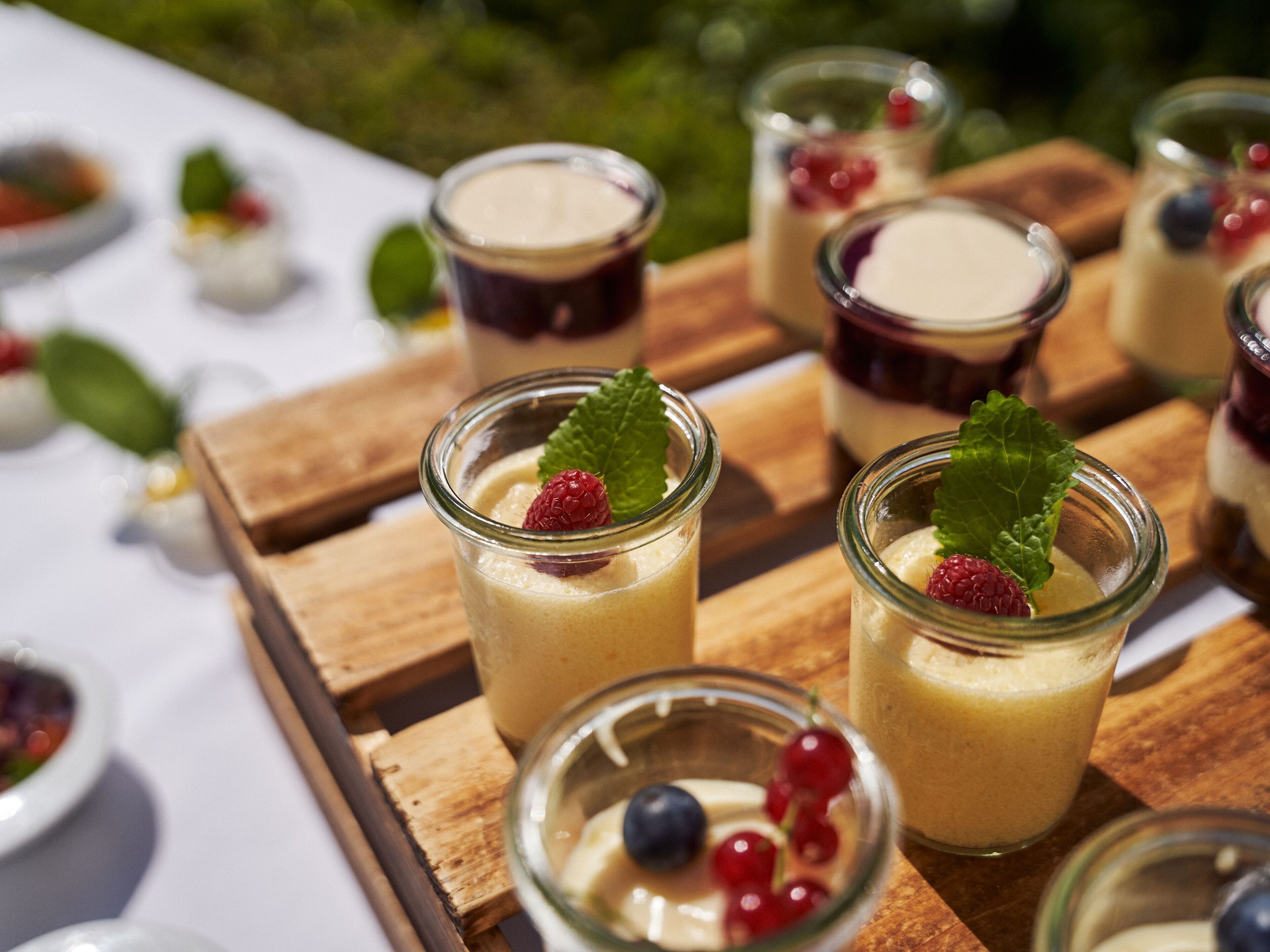 Ein Tisch mit mehreren kleinen Glaskonstruktionen, gefüllt mit Dessert, jede mit einer Beere und einem Minzblatt dekoriert.