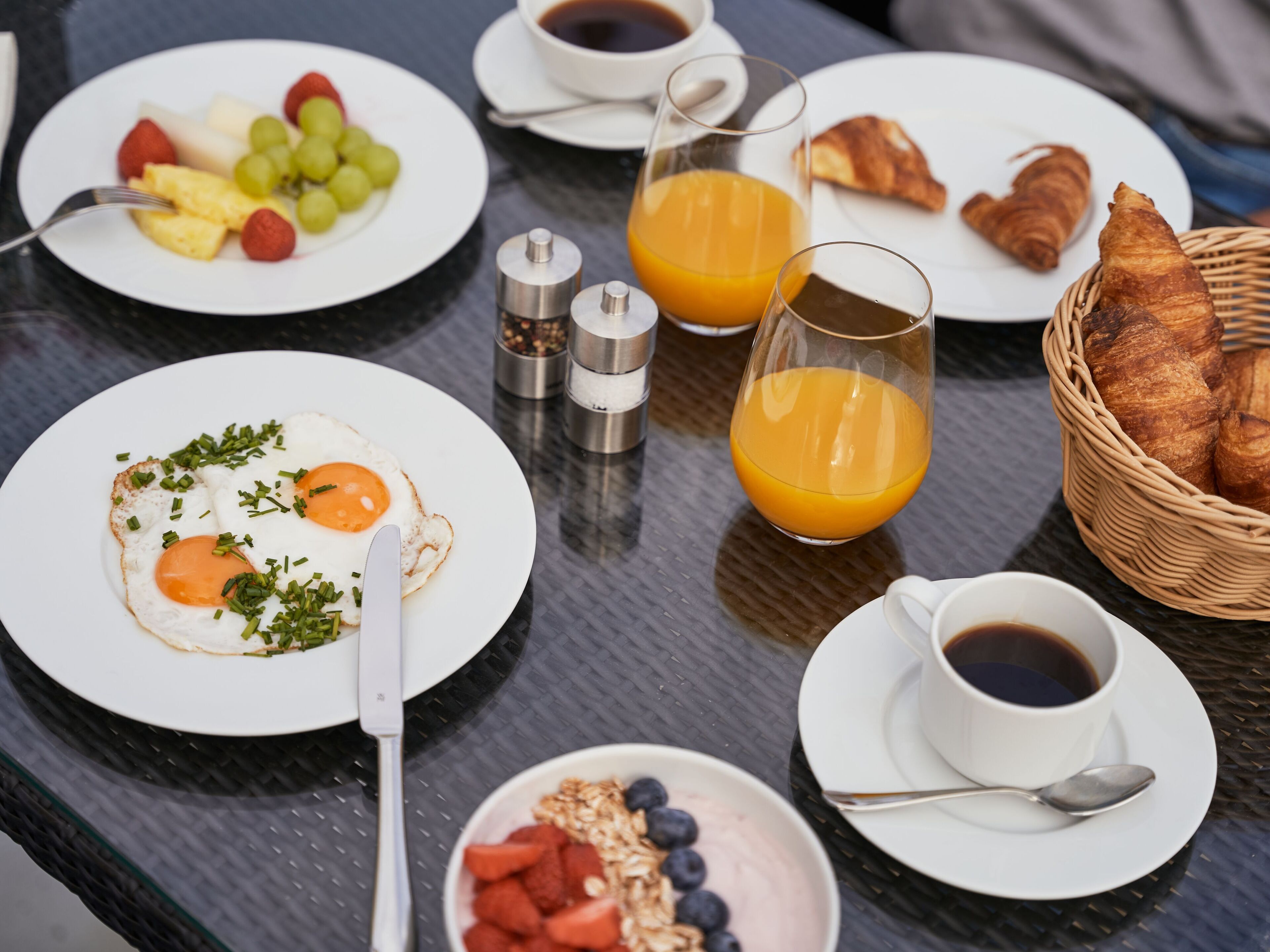 Une table de petit-déjeuner avec des assiettes d’œufs, des fruits, des croissants et du jus d’orange.