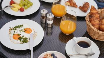 A breakfast table with plates of eggs, fruit, croissants, and orange juice.