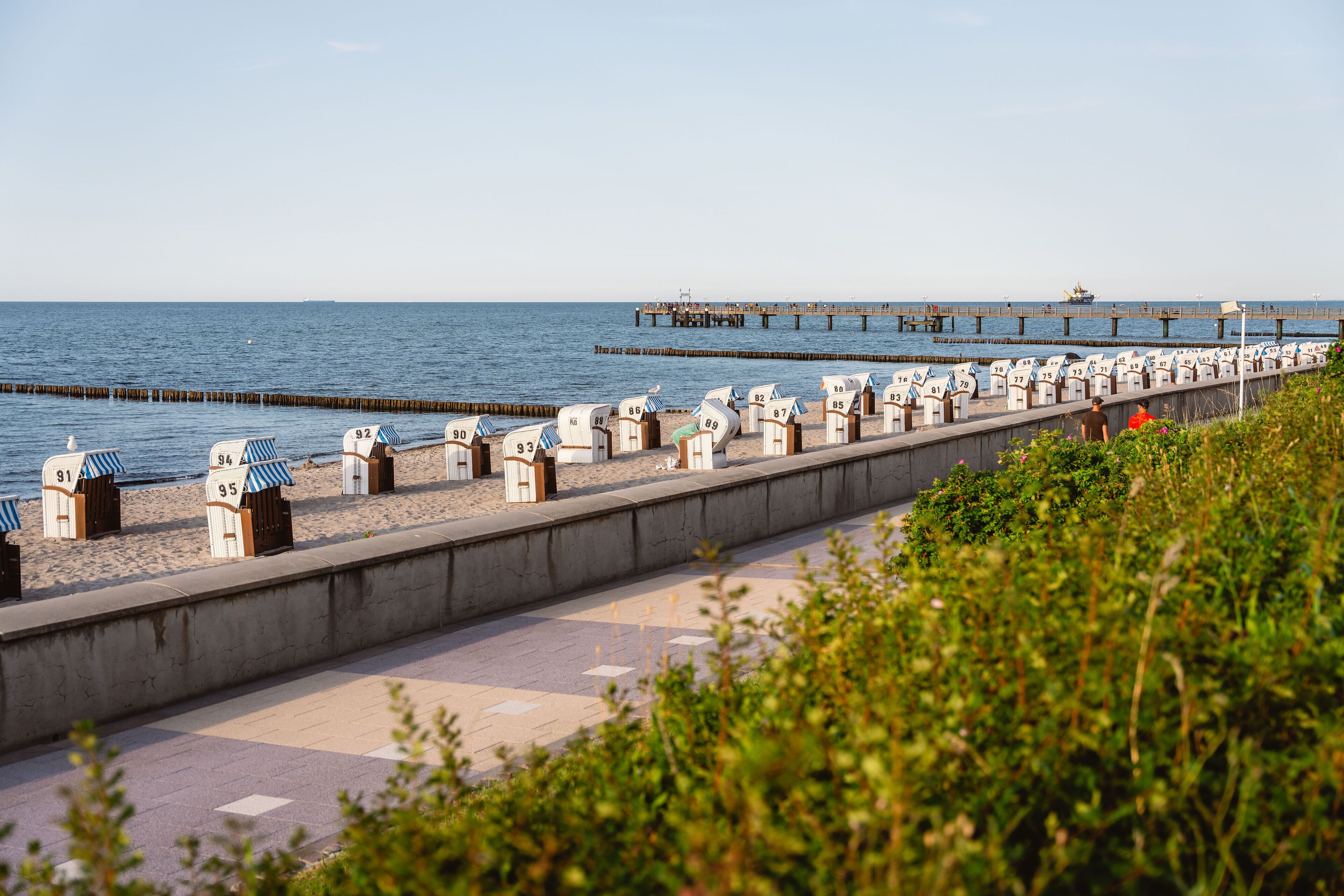 Eine Uferpromenade mit nummerierten Strandkörben und einem Pier im Hintergrund.