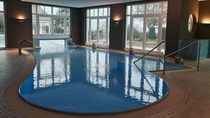Una piscina interior con paredes de vidrio transparente, suelo de baldosas y diseño curvo.