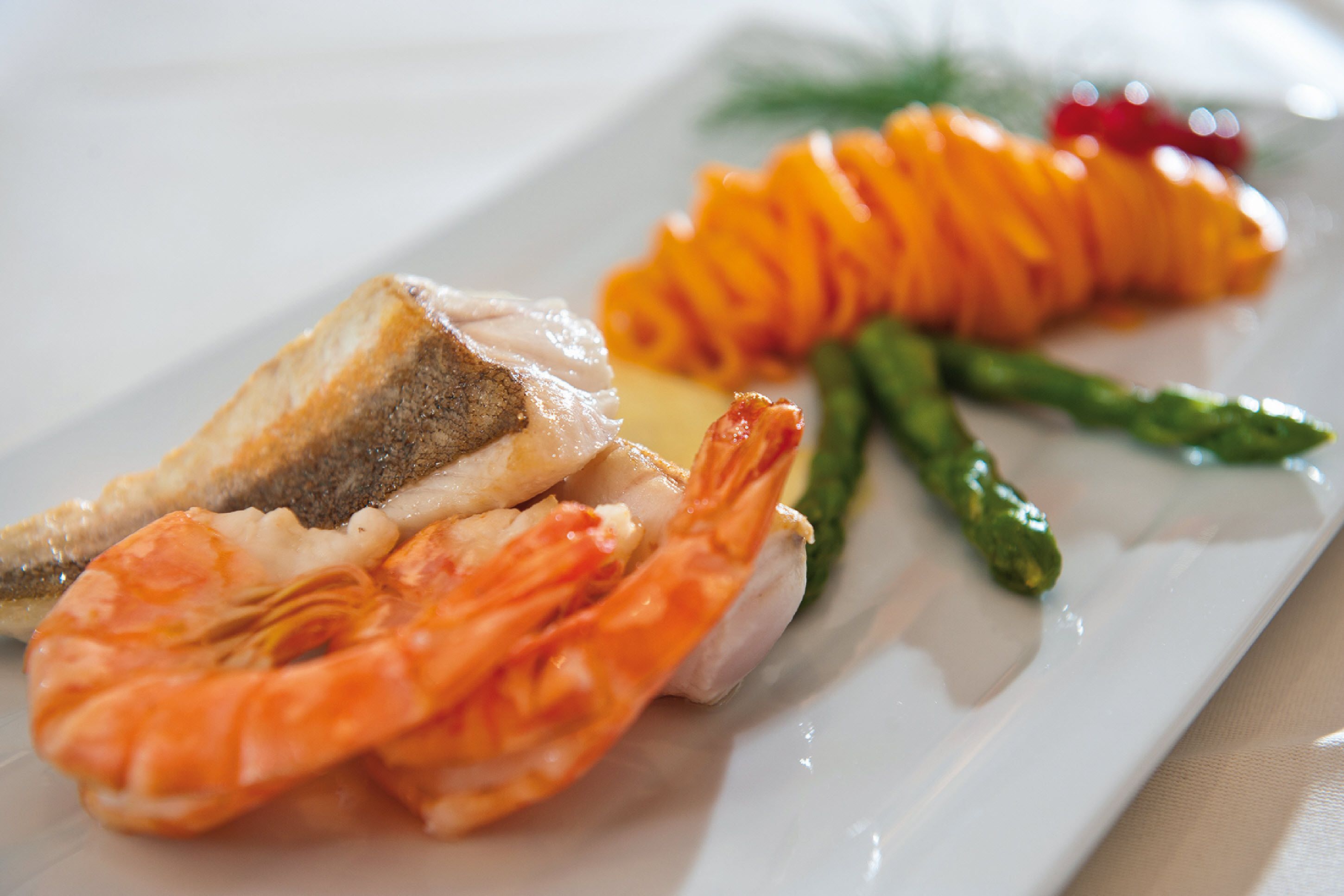 A plate with a slice of bread, a piece of fish, a shrimp, and some asparagus.