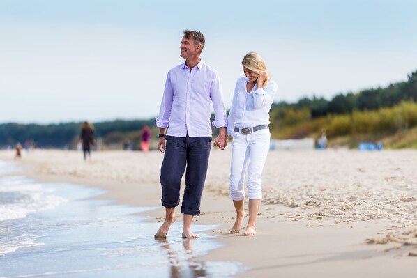 A couple walking on a sandy beach with a clear sky.