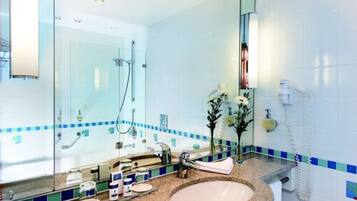 A bathroom with a glass-enclosed shower, a sink with a mirror, and a telephone.