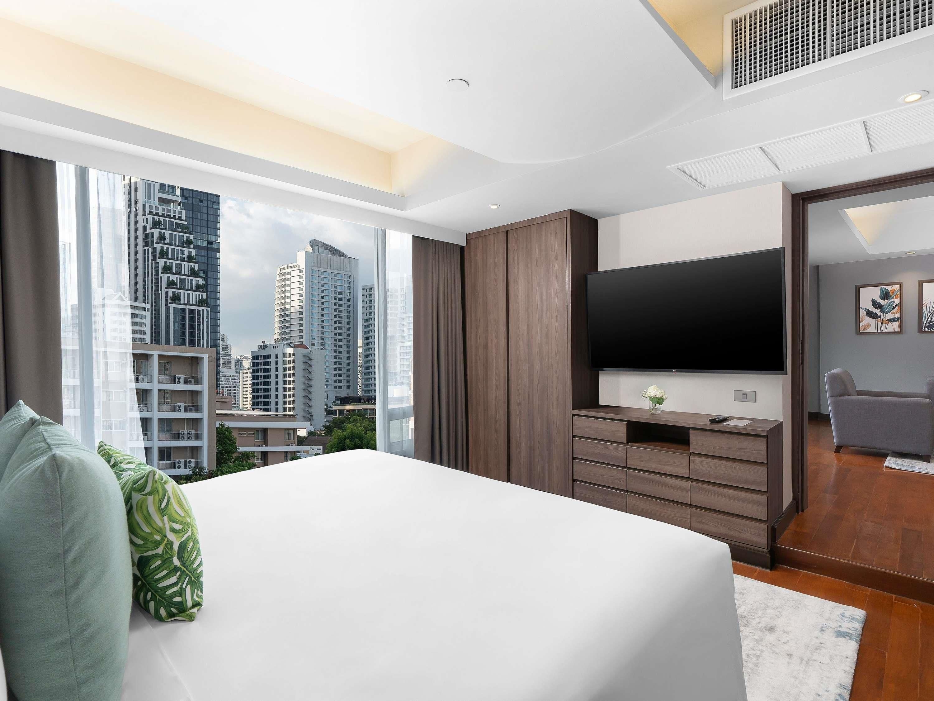 A modern hotel room with a large bed, a flat-screen TV, a wooden wardrobe, and a city view.