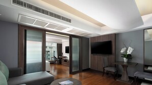 A modern hotel room with a sofa, a coffee table, a TV, and a small table with flowers.