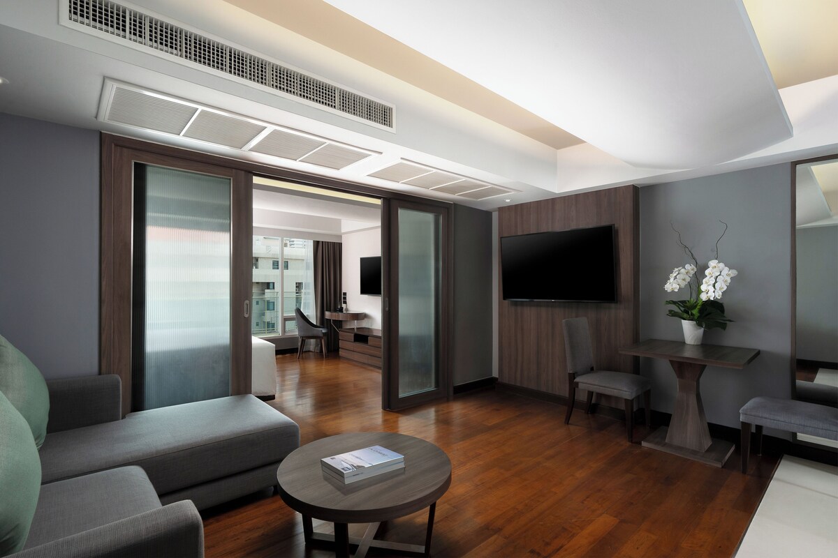 A modern hotel room with a sofa, a coffee table, a TV, and a small table with flowers.