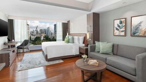 A modern hotel room with a large bed, a sofa, a coffee table, and a TV. - Novotel Living Bangkok Sukhumvit Legacy (Bangkok)