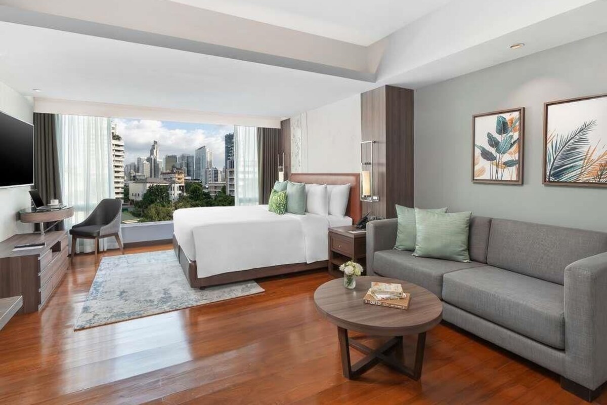 A modern hotel room with a large bed, a sofa, a coffee table, and a TV.
