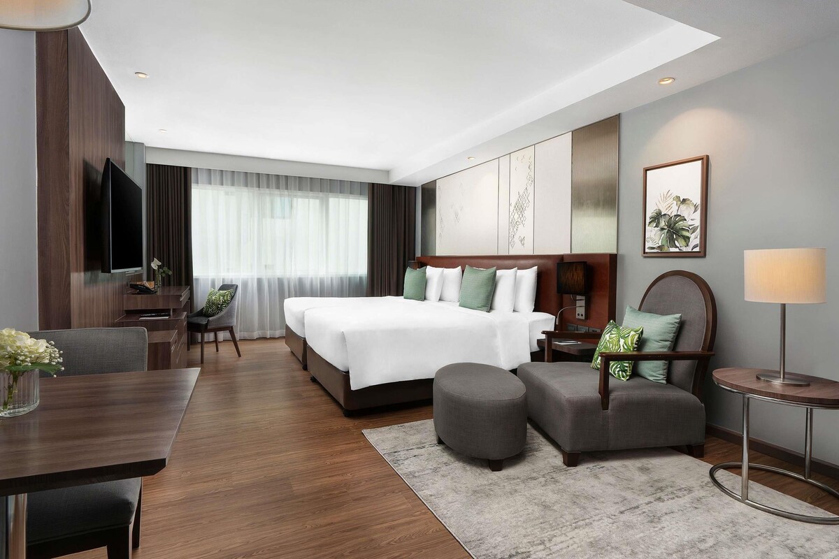 A modern hotel room with a large bed, a desk, a chair, a TV, and a window with curtains.