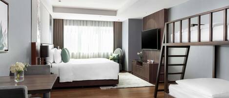 Habitación de hotel con cama, escritorio, televisor y literas.