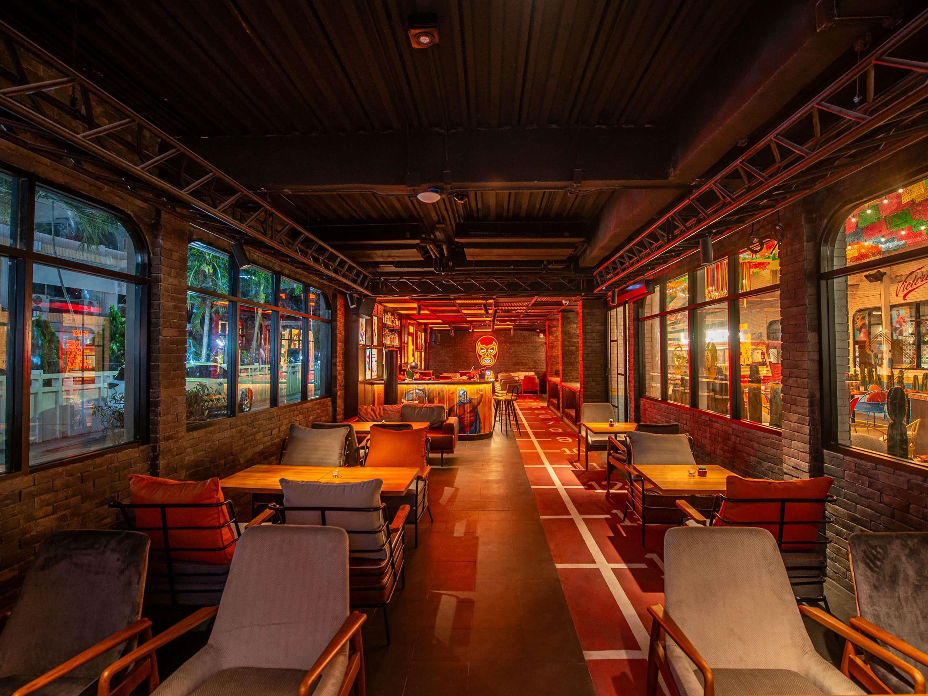A restaurant interior with brick walls, large windows, and a central bar area.